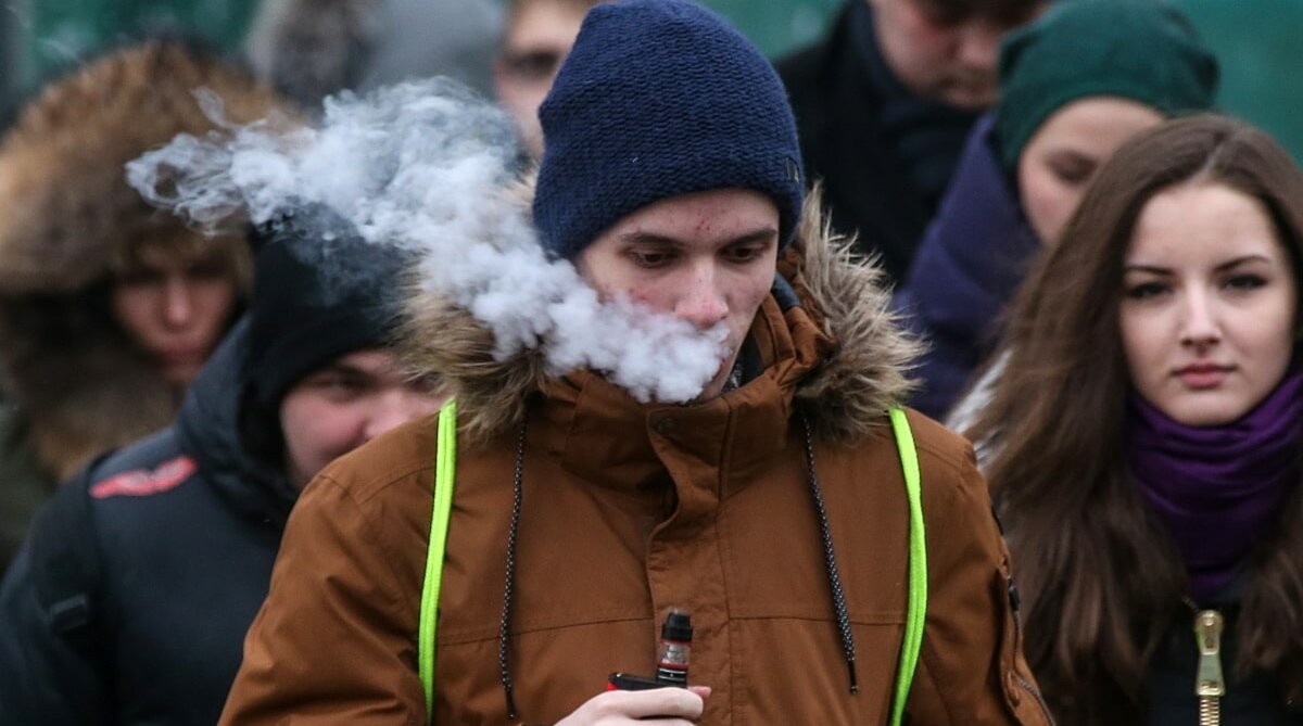 Молодой человек курит электронную сигарету, вейп